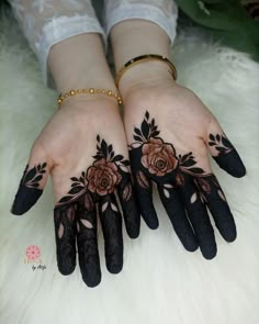 two hands with black and brown henna tattoos on them, one is holding the other's hand