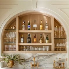 a marble counter top with gold faucets and liquor bottles on the shelves above it