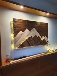 a wooden wall hanging on the side of a building with lights around it and mountains in the background