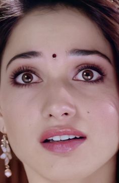 a close up of a woman with brown eyes and piercings on her head, wearing pearls