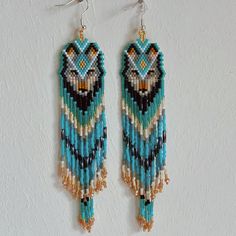 two pairs of beaded owl earrings hanging from hooks on a white wall, one with blue and brown beads