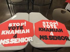 two red and white signs sitting on top of tables in a room filled with chairs