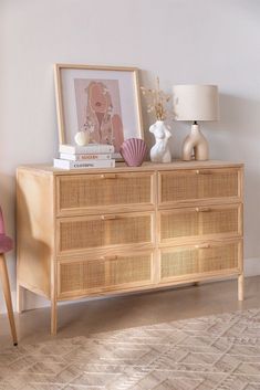 a wicker dresser with books, vases and pictures on it in front of a white wall