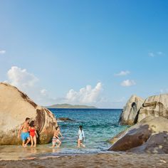 three people are wading in the water near large rocks and boulders on the beach