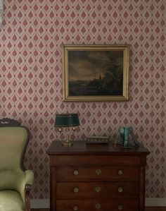 a chair sitting next to a dresser in a room with wall paper on the walls