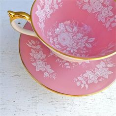 two pink and gold teacups sitting on top of each other with flowers painted on them