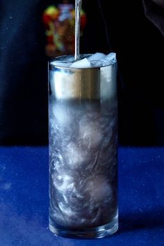 a person pouring something into a glass with ice in it on a blue table top