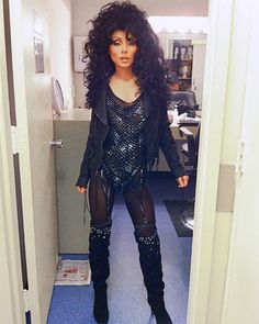 a woman with long black hair and boots standing in a doorway wearing an outfit that has sequins on it