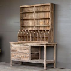 an old wooden desk with drawers and shelves on the top, in front of a gray wall