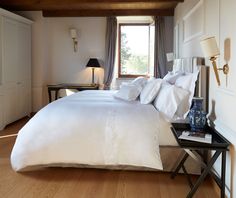 a bed with white sheets and pillows in a bedroom next to a lamp on a table