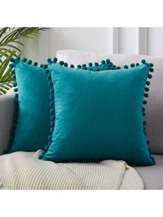 two pillows with pom poms on them, one blue and the other white