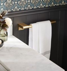 a vase with flowers in it sitting on a bathroom counter next to a towel rack