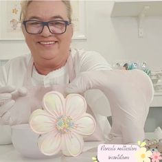 a woman in white gloves and glasses holding a flower shaped cookie on top of a table