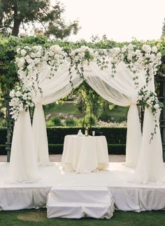 an outdoor wedding setup with white flowers and draping on the back drop cloths