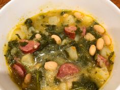 a white bowl filled with soup and beans on top of a wooden table next to a spoon