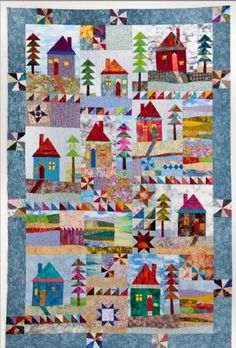 a quilted wall hanging with houses and trees in the center, on top of a blue background