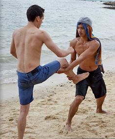 two young men practicing martial moves on the beach