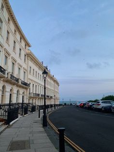 an empty street lined with parked cars next to tall white buildings on either side of the road