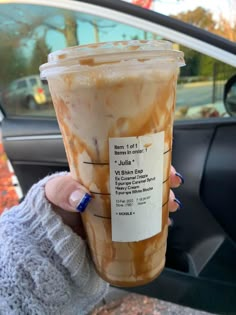 a woman holding up a cup of iced coffee in front of her car door window