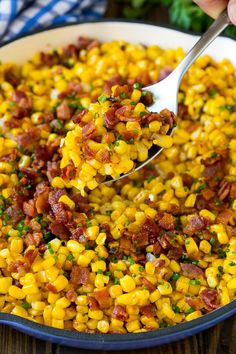 a spoon full of corn with bacon and parsley on top in a skillet