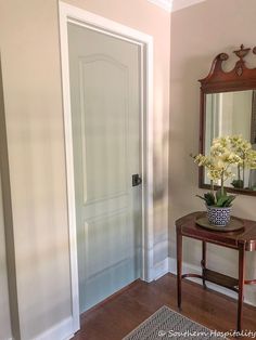 a vase with white flowers on a table in front of a mirror and door to another room