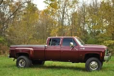 a red pick up truck parked on top of a lush green field next to trees