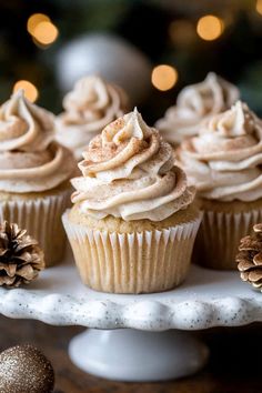 cupcakes with frosting and pine cones on a white cake plate next to christmas decorations