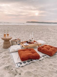 an outdoor picnic setting on the beach with food and drinks laid out in front of it