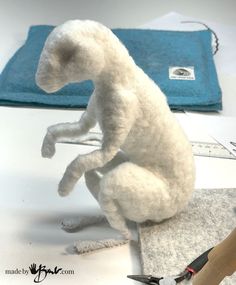 a white stuffed animal sitting on top of a table next to scissors and tape measure