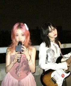 two young women with pink hair are holding guitars and looking at their cell phones while standing next to each other