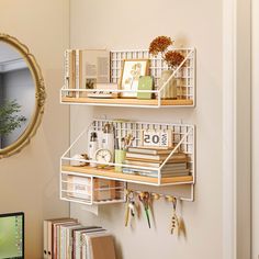 two white shelves with books, magazines and other items on them in front of a mirror