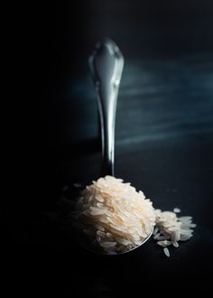 a spoon filled with rice on top of a black table next to a pile of rice