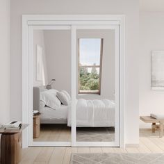 a bedroom with white walls and wooden floors, large sliding glass doors leading to the outside