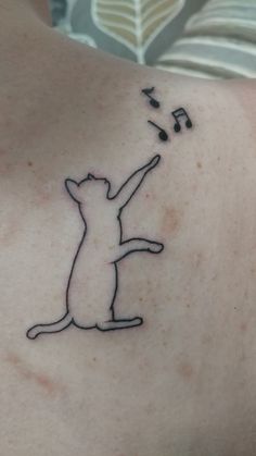 a person with a cat tattoo on their back holding a musical note in the air