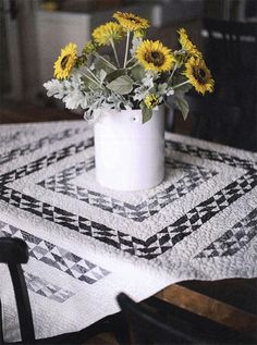 sunflowers in a white vase on a quilted tablecloth at a dining room table