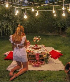 a woman sitting on the grass in front of a picnic table