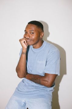 a man sitting down with his hand on his chin and looking at the camera while wearing a blue t - shirt