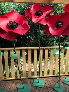 three large red flowers sitting on top of green bases in front of a wooden fence