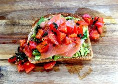 a sandwich with tomatoes, avocado and other toppings sitting on a cutting board