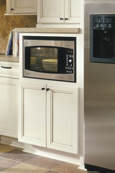 a stainless steel microwave oven in a kitchen with white cupboards and tile flooring