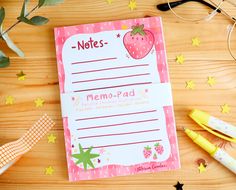 a notepad sitting on top of a wooden table next to some pens and scissors