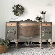 an old dresser is painted gray and gold with flowers on the top, along with potted plants