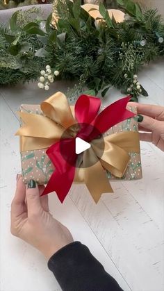 someone is holding a gift wrapped in gold and red ribbon with a bow on it