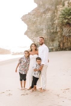 a man and two children standing on the beach in front of some cliffs at sunset