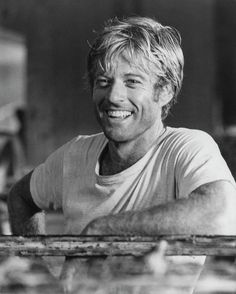 a smiling man sitting at a table with his arms crossed and looking off to the side