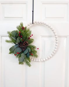 a wreath hanging on the front door decorated with greenery and pineconis for christmas