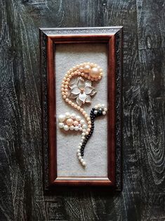 a frame with pearls and flowers in it on a wooden table next to a wall