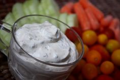 a bowl of dip surrounded by carrots, celery and oranges on a table