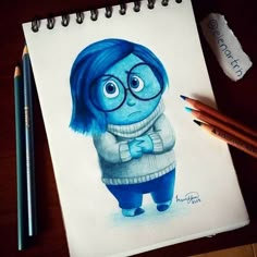 a drawing of a blue monster with glasses and a sweater on, next to two colored pencils