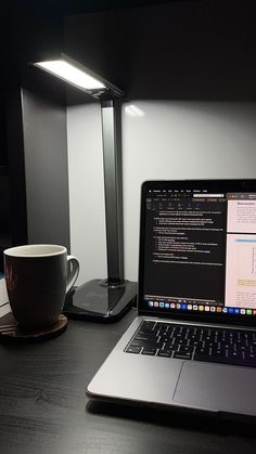 an open laptop computer sitting on top of a wooden desk next to a cup of coffee